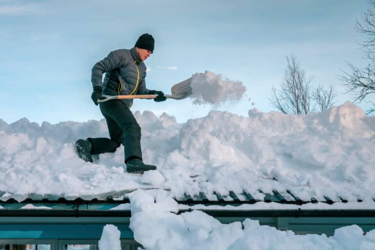 Handsome Caucasian teenager with shovel remove snow from roof of